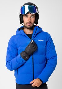 Sininen eristetty hiihtotakki, jossa on huppu, vetoketjukiinnitys ja joustavat hihansuut. Mallilla on mustat käsineet ja kypärä, jossa on suojalasit. Suunnittelijan logo näkyvillä.