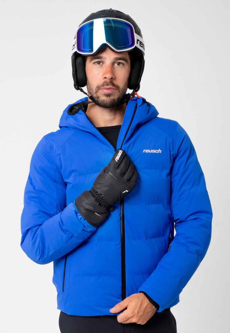 Sininen eristetty hiihtotakki, jossa on huppu, vetoketjukiinnitys ja joustavat hihansuut. Mallilla on mustat käsineet ja kypärä, jossa on suojalasit. Suunnittelijan logo näkyvillä.