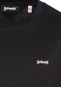 Čierne bavlnené tričko s okrúhlym výstrihom, ktoré má malé biele vyšívané logo "Schott" a štítok s veľkosťou L.