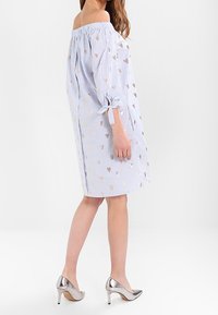 Axelklänning i ljusblått med vita ränder och metalliska hjärtaccenter. Har knytdetaljer på ärmarna och en lös passform.