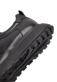 Sneaker nera con tomaia in pelle e suola in gomma testurizzata con profonde scanalature per una buona trazione. Include un'apposita linguetta al tallone.