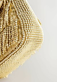 Goldene Handtasche mit einer strukturierten Oberfläche. Besetzt mit glänzenden Pailletten, die in Mustern angeordnet sind und ein komplexes Design schaffen. Runde Form mit einer sanften Oberfläche.