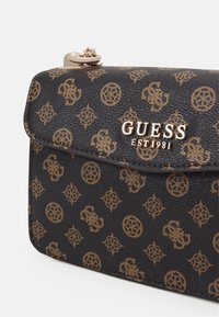 Black textured synthetic leather clutch with geometric and logo patterns, featuring a gold-tone clasp and "GUESS EST 1981" branding.