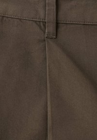 Gros plan sur un pantalon en tissu marron montrant la ceinture, la boucle de ceinture et la couture centrale avec des détails de couture visibles.