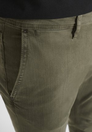 Olivgrüne Hose aus strukturiertem Stoff mit sichtbaren Nähten und seitlichen Taschen; mit einem kleinen braunen Knopf befestigt.