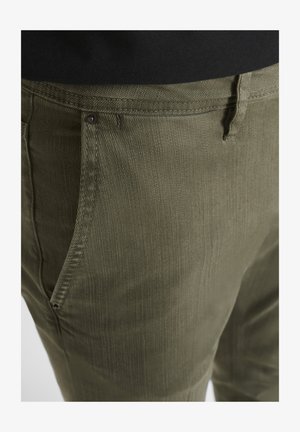 Hlače maslinaste boje napravljene od strukturirane tkanine s vidljivim šavovima i bočnim džepovima; zatvorene malim smeškim dugmetom.