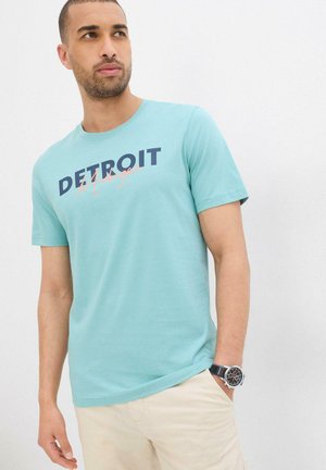 T-shirt di cotone turchese con una grafica audace in navy "DETROIT" e un accento arancione chiaro. Maniche corte e scollatura rotonda.