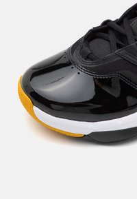 Lesklé černé tenisky s texturovanou látkou, žlutou gumovou podrážkou, bílou mezipodešví a černými tkaničkami. Vyznačují se zaoblenou špičkou a elegantním designem.