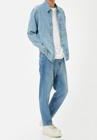 Světle modrá džínsová košile s knoflíky, spárovaná se světle modrými rovnými džíny a bílými teniskami. Minimalistický design, volný střih.