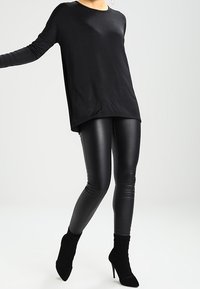 Schwarz-langärmliges Oberteil mit lockerer Passform, kombiniert mit glänzenden schwarzen Leggings und spitzen Ankle Boots, alles in einem eleganten, monochromatischen Stil.