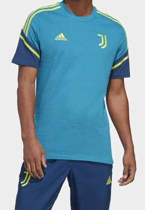 Mann trägt blaue und marineblaue Juventus-Sportbekleidung mit neon-gelben Adidas-Logos und Streifen auf Shirt und Hose.