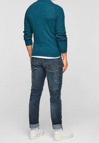 Maglione lavorato a maglia color verde acqua con polsini a costine, abbinato a jeans blu scuro con effetto slavato e risvolti sulle caviglie. L'outfit è completato da sneakers bianche.