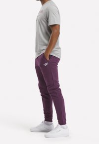 Gray cotton t-shirt with "Reebok" logo, paired with purple sweatpants featuring side pockets, and white athletic shoes.