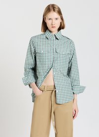 Green and white checkered shirt with a button-down collar, two chest pockets, and rolled-up sleeves, paired with tan pants.