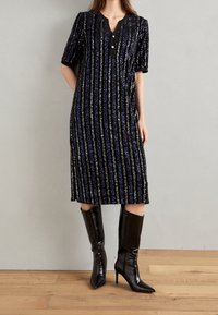 Svart midiklänning med vertikala blå och silverfärgade paljetter, v-ringning, korta ärmar och en knappdetalj vid halslinningen.