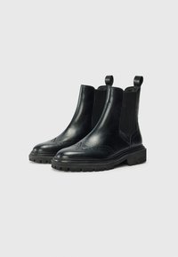 Bottines noires en cuir avec une finition lisse, des détails de brogue, des panneaux élastiques sur les côtés et des semelles à crampons pour une meilleure traction. Comprend des languettes de tirage.