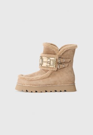 Bota de camurça clara com colarinho de pelo sintético, fivela decorativa com gemas e sola de borracha com padrões em ziguezague e um detalhe semelhante a um cristal.