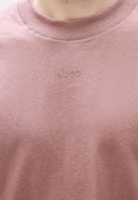 Růžové bavlněné tričko s ribovaným výstřihem, na hrudi s malým embosovaným logem "HUGO". Měkká textura a ležérní design.