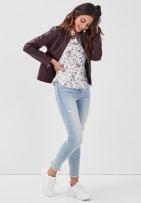 Veste en cuir bordeaux sur un chemisier floral blanc, associée à un jean skinny déchiré bleu clair et des baskets blanches à semelles épaisses.