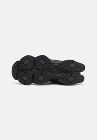 Black athletic shoe sole with a textured rubber surface, featuring hexagonal and diamond-shaped patterns for traction and grip.