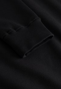Tissu de sweat-shirt noir avec un poignet côtelé, présentant une texture lisse et un design simple, capturant le détail de l'attache du vêtement.
