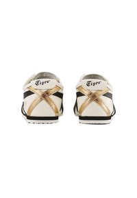 White sneakers with black stripes and a gold metallic cross pattern on the heel. "Tiger" logo on the back, rubber soles, and no laces.