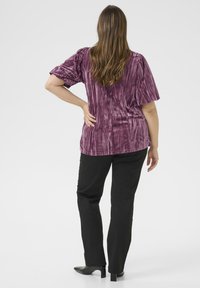 Haut court en velours violet froissé associé à un pantalon noir et des bottines, mettant en avant une coupe décontractée et un design texturé.