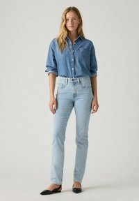 Jeans de denim azul claro con cintura alta, combinados con una camisa de chambray azul a juego. La modelo lleva zapatos planos negros, de corte clásico.
