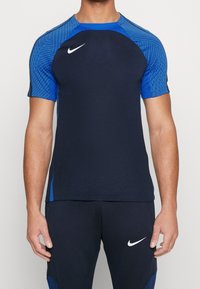 Marinblå sporttröja med mönstrade ärmar i blått. Tillverkad av andningsbart material, har rund halsringning och Nike-logotypen på bröstet.