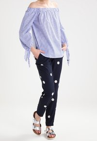 Blusa a rayas azul y blanca, con los hombros al descubierto y mangas con lazo, combinada con pantalones azul marino con puntos blancos; modelo lleva sandalias plateadas.