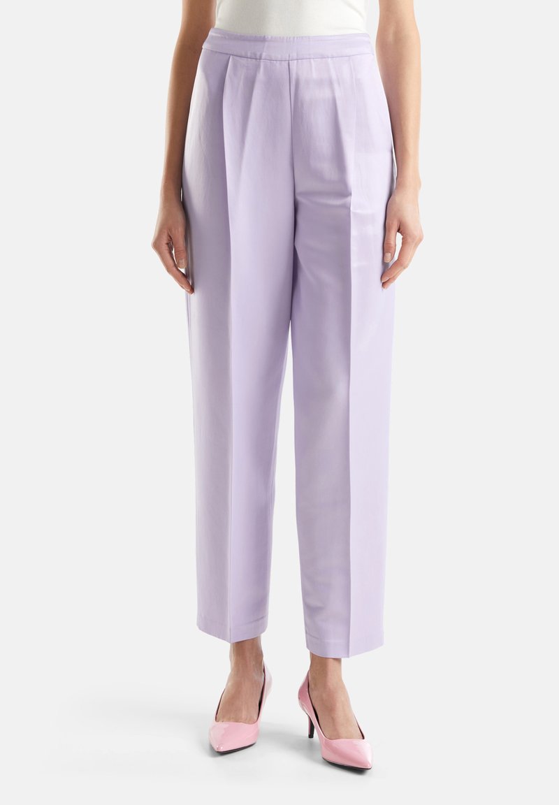 Pantaloni a vita alta lilla con pieghe, dalla vestibilità ampia e texture morbida. Abbinati a tacchi alti rosa lucidi.