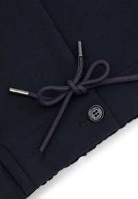 Navy materiał pikowany z produktem wyposażonym w sznurek ściągający z metalowymi końcówkami oraz logo w formie okrągłego guzika. Teksturowana powierzchnia, prosty design.