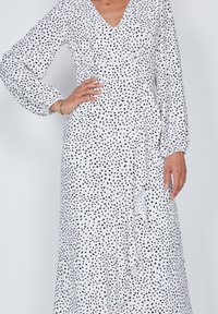Vestido blanco con escote en V y mangas largas abullonadas, con un patrón de puntos abstractos en negro, tela suave y detalle de cintura ajustada.