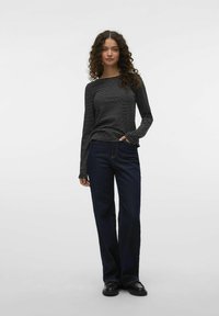 Zwart-wit gestreepte shirt met lange mouwen gecombineerd met donkerblauwe wijde jeans en zwarte schoenen. Eenvoudig, casual ontwerp met een losse pasvorm.