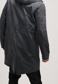 Manteau long gris foncé avec capuche, doté d'une finition texturée, de poches latérales et d'un ourlet arrière légèrement allongé pour une couverture supplémentaire.