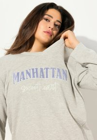 Felpa grigia con "MANHATTAN" ricamato in blu e "sweetheart" in bianco corsivo. Caratterizzata da una vestibilità ampia e maniche lunghe.