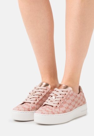 Lyserøde lavtop-sneakers med mønster og hvide platformsåler, båret på fødder, med metallisk roseguld tunge og snørehuller.