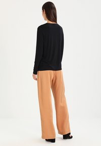 Top nero a maniche lunghe abbinato a pantaloni beige a gamba larga; entrambi i capi presentano texture morbide e lisce e vestibilità rilassata.