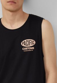 Schwarzes ärmelloses Shirt mit rundem Ausschnitt und einem großen, in Hellrosa gedruckten Logo, das "PACIFIC CUSTOMS BOARDS&KITS" liest.