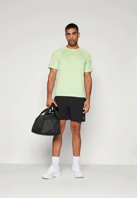 Light green athletic t-shirt, black shorts, and white sneakers. Black gym bag with dual handles. Smooth fabric and casual fit.