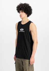 Μαύρο αμάνικο μπλουζάκι φτιαγμένο από βαμβάκι. Διαθέτει λευκό λογότυπο "ALPHA INDUSTRIES" στο στήθος. Απλός σχεδιασμός με στρογγυλή λαιμόκοψη.