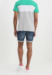 Camiseta bloqueada en gris y verde, pantalones cortos de mezclilla con los dobladillos enrollados y zapatillas blancas con acentos rojos.