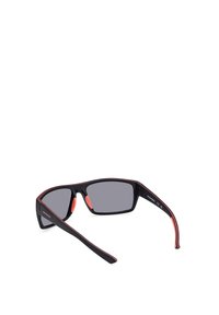 Gafas de sol con montura negra, detalles rojos, lentes grises y almohadillas de goma en la nariz. Presentan un diseño deportivo con brazos curvados y un acabado mate.