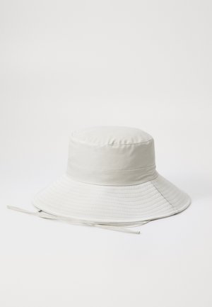 Chapéu de balde branco feito de tecido suave, com uma aba larga e flutuante, apresentando detalhes costurados e uma fita para o queixo.