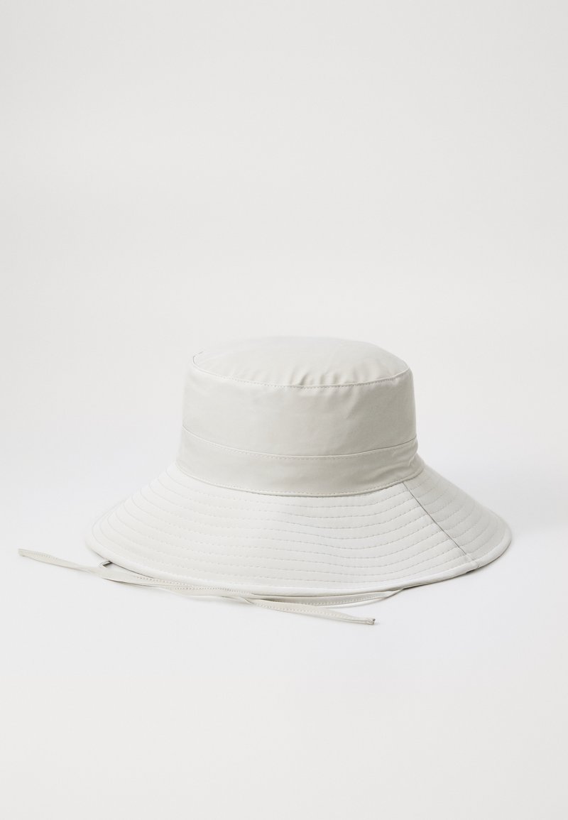 Chapeau seau blanc en tissu lisse avec un large bord évasé, présentant des détails cousus et une sangle sous le menton.