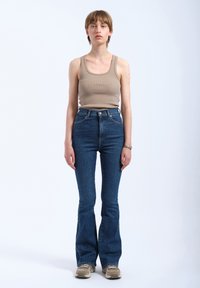 Beige ribbed tank top paired with high-waisted blue flared jeans. The outfit is completed with light-colored sneakers.