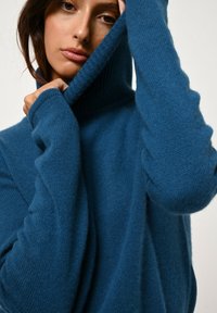 Blå stickad tröja med hög ribbad krage och långa, något oversized ärmar. Texturerad tyg ger mjukhet och värme.