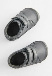 Chaussures en cuir gris avec deux bandes Velcro, présentant une surface texturée et un bout rond. La semelle est douce, conçue pour le confort.