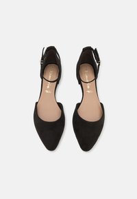 Paire de ballerines en daim noir à bout pointu avec bride à la cheville à boucle et semelles intérieures beiges sur fond uni.
