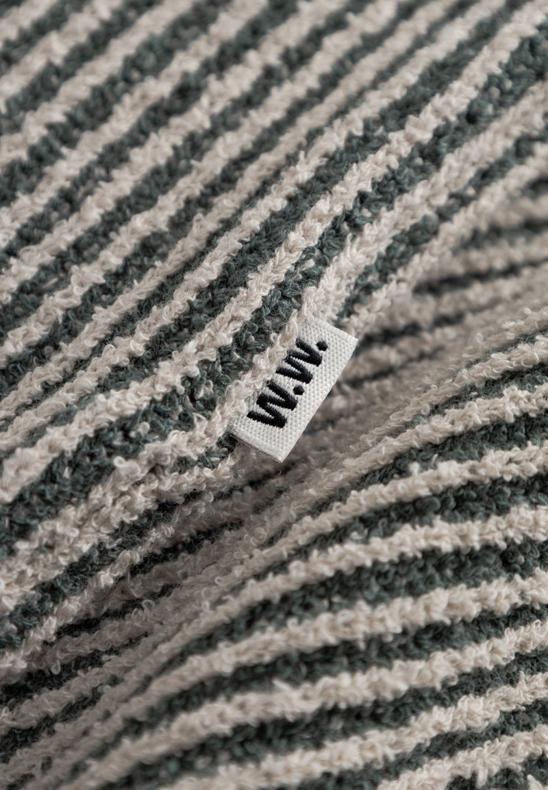 Cotton blanket with alternating green and cream stripes, textured surface, and a small fabric tag with black lettering.
